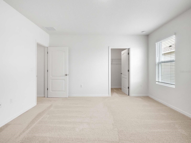 unfurnished bedroom featuring a walk in closet, a closet, and light carpet