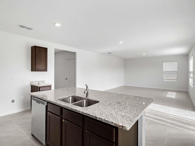 kitchen with stainless steel dishwasher, sink, light stone counters, a kitchen island with sink, and light tile patterned flooring