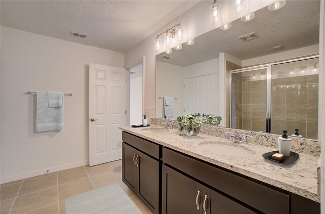 bathroom with tile patterned flooring, double sink vanity, a textured ceiling, and a shower with shower door