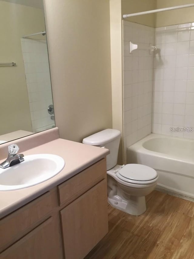 full bathroom featuring toilet, tiled shower / bath, vanity, and wood-type flooring