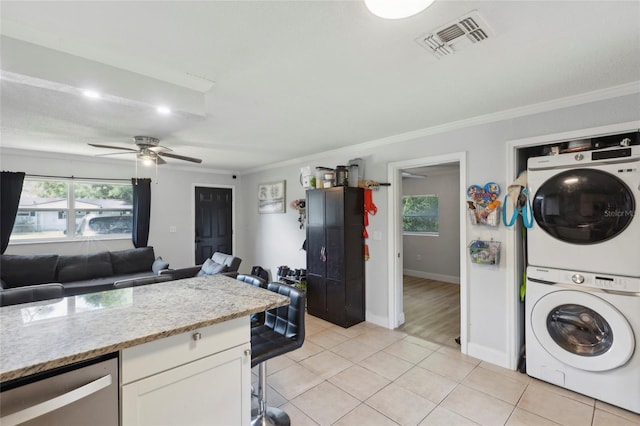 kitchen featuring stacked washing maching and dryer, white cabinetry, ceiling fan, light tile patterned floors, and crown molding