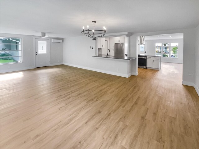 unfurnished living room with sink, light wood-type flooring, a wall unit AC, and a chandelier