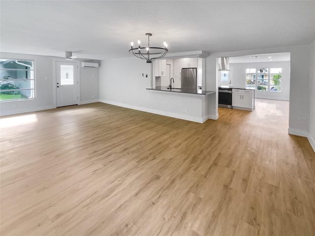 unfurnished living room with a notable chandelier, light wood finished floors, a wall mounted AC, a sink, and baseboards