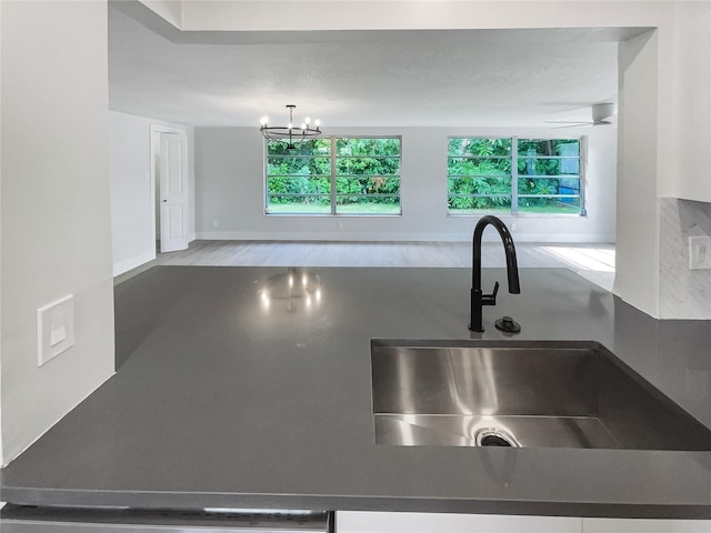 kitchen with a sink, baseboards, light wood finished floors, dark countertops, and an inviting chandelier