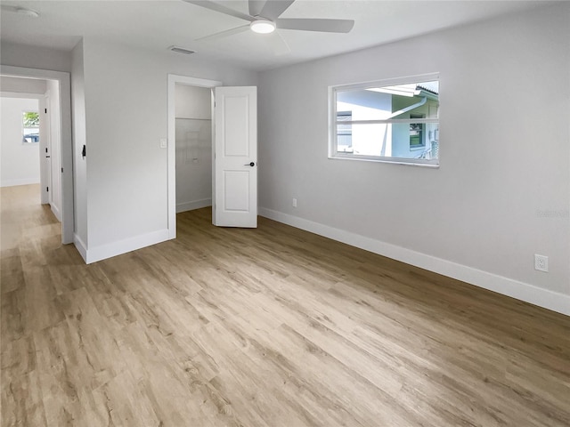 unfurnished bedroom featuring baseboards, visible vents, a ceiling fan, a walk in closet, and light wood-style floors