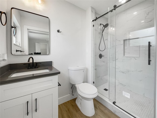 bathroom featuring a marble finish shower, baseboards, toilet, wood finished floors, and vanity