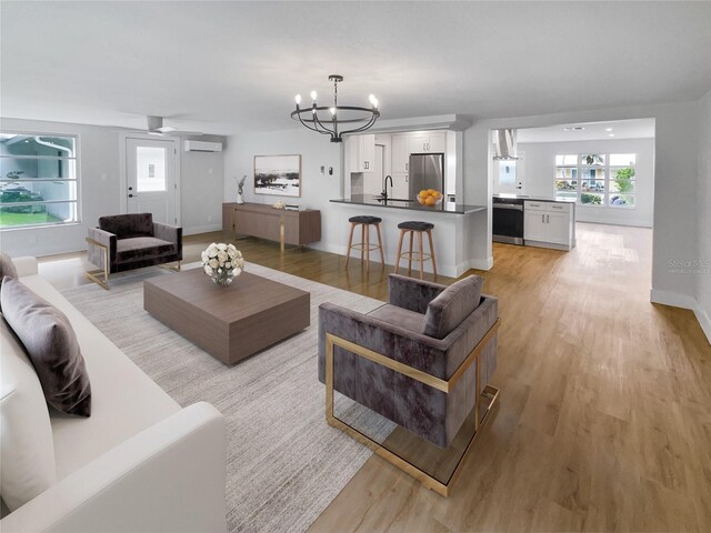 living room with sink, light wood-type flooring, a wall mounted AC, and a notable chandelier