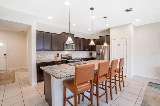 kitchen featuring a kitchen island with sink, stainless steel appliances, a breakfast bar, visible vents, and decorative light fixtures