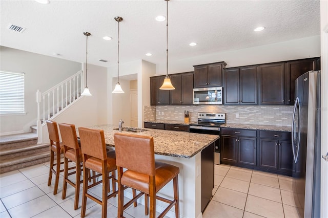 kitchen with pendant lighting, light tile patterned floors, stainless steel appliances, a kitchen island with sink, and a kitchen breakfast bar