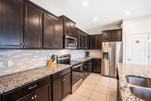 kitchen featuring light stone counters, light tile patterned flooring, dark brown cabinetry, stainless steel appliances, and tasteful backsplash