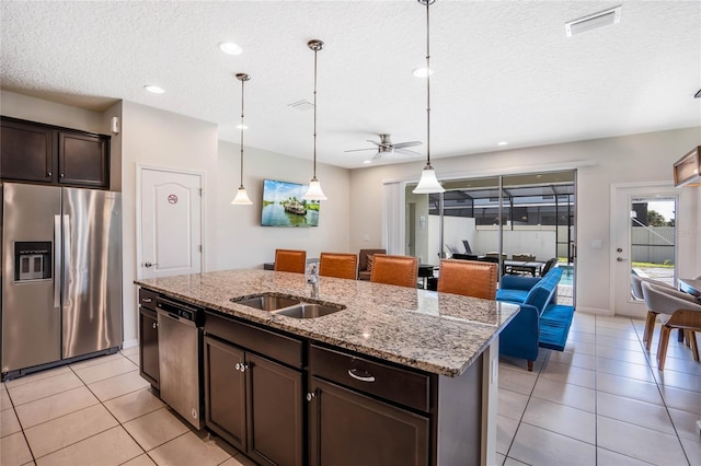 kitchen with decorative light fixtures, a center island with sink, stainless steel appliances, a sink, and dark brown cabinets