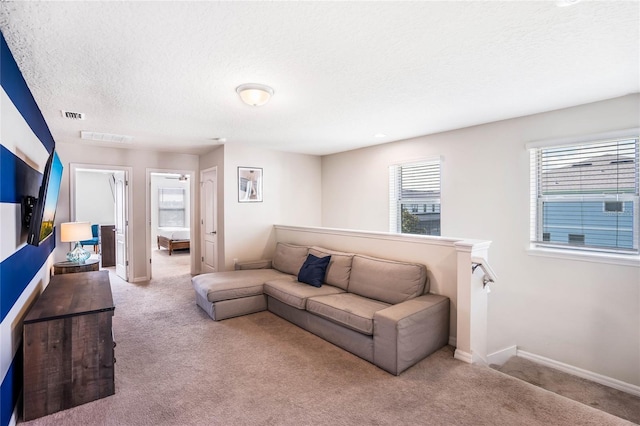 living area with baseboards, visible vents, a textured ceiling, and light colored carpet