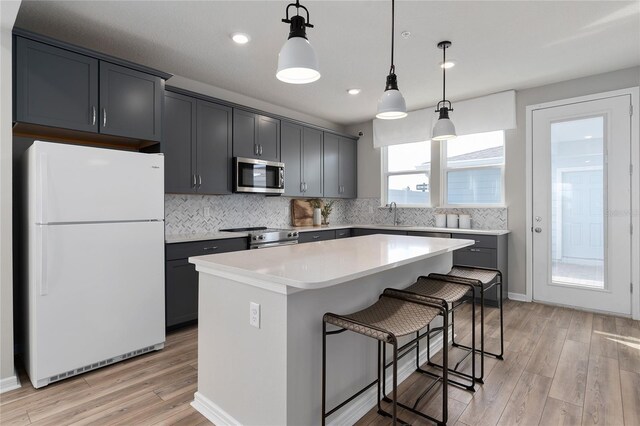 kitchen with decorative backsplash, a kitchen island, hanging light fixtures, appliances with stainless steel finishes, and light hardwood / wood-style floors