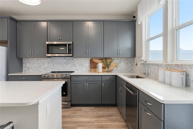 kitchen with sink, decorative backsplash, light hardwood / wood-style floors, gray cabinetry, and stainless steel appliances