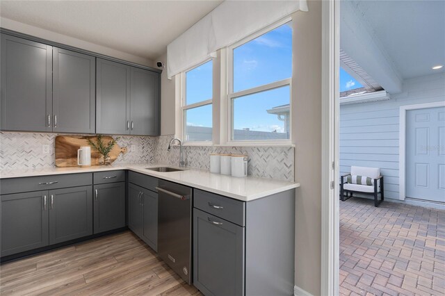 kitchen with decorative backsplash, light hardwood / wood-style flooring, stainless steel dishwasher, gray cabinets, and sink