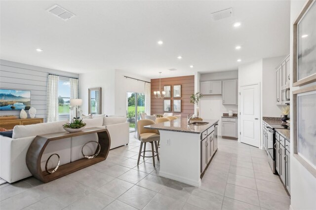 kitchen with light tile patterned floors, sink, a center island with sink, and stainless steel range with electric stovetop