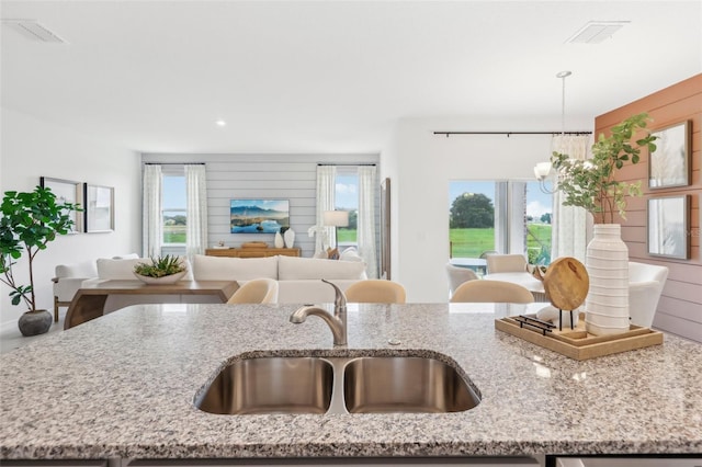 kitchen featuring sink, hanging light fixtures, light stone countertops, and an inviting chandelier