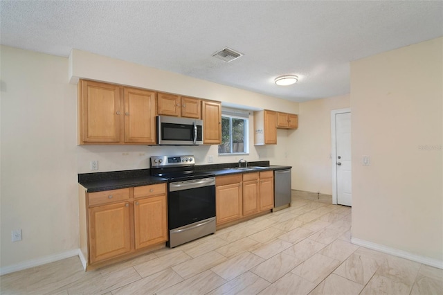 kitchen with sink, a textured ceiling, light tile patterned floors, and stainless steel appliances