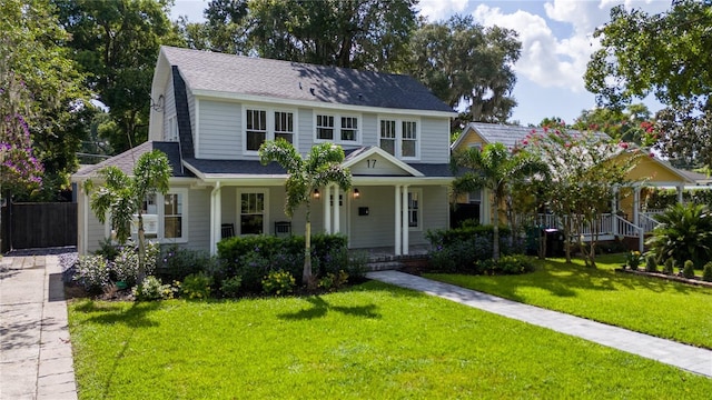 view of front of home with covered porch, a shingled roof, and a front yard