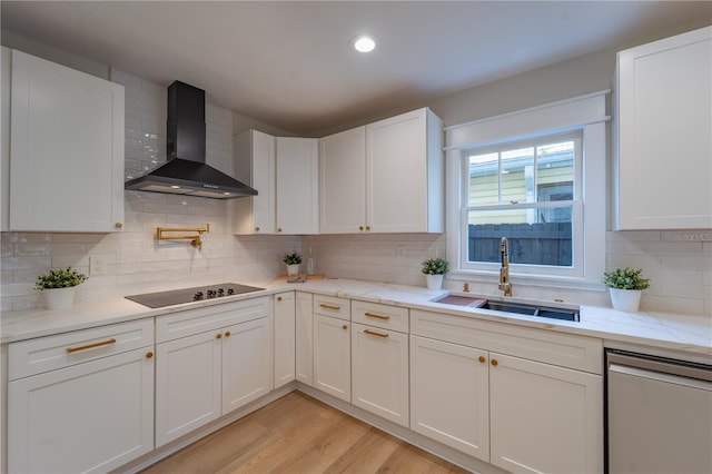 kitchen featuring light stone counters, black electric stovetop, white cabinetry, a sink, and wall chimney exhaust hood