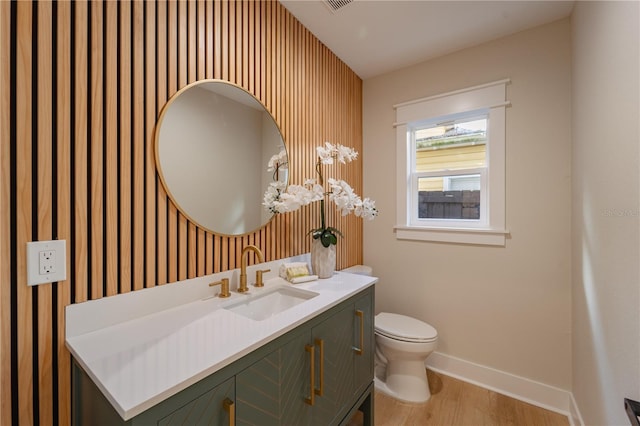 half bath featuring toilet, wood finished floors, visible vents, vanity, and baseboards