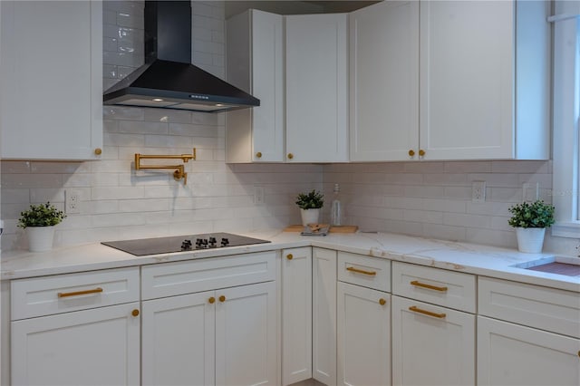 kitchen with black electric cooktop, wall chimney exhaust hood, white cabinets, and backsplash