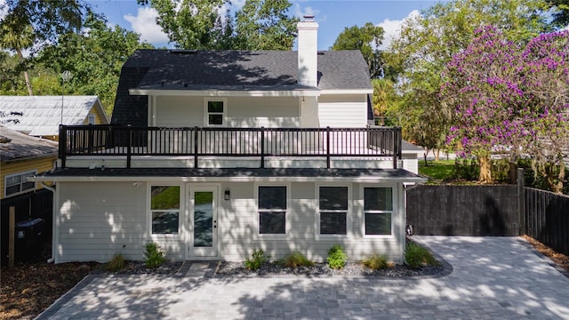 rear view of house featuring a shingled roof, a chimney, fence, and a balcony