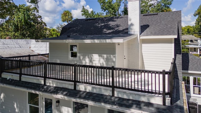 back of house featuring a shingled roof, a chimney, and a balcony