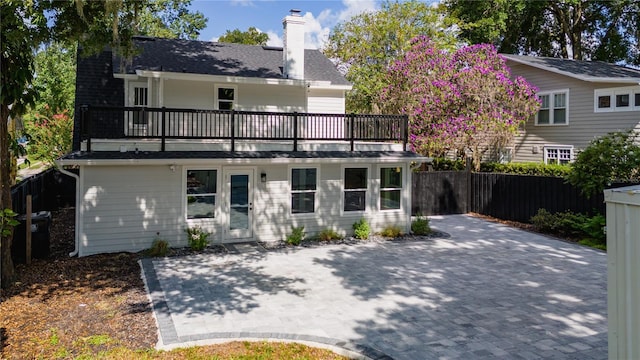 back of house with a chimney, a patio area, fence, and a balcony