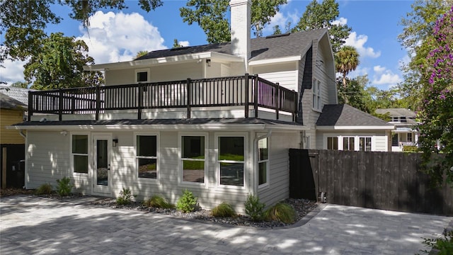 view of front of house featuring a chimney, roof with shingles, fence, and a balcony