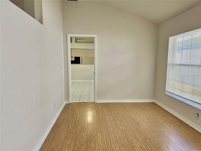 spare room with light wood-type flooring, a wealth of natural light, lofted ceiling, and baseboards