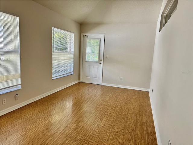 empty room with lofted ceiling, light wood-style flooring, baseboards, and a textured ceiling