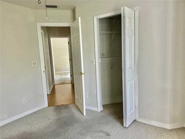 unfurnished bedroom with a closet, visible vents, light carpet, and baseboards