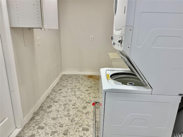 clothes washing area with baseboards, laundry area, stacked washing maching and dryer, and stone finish flooring