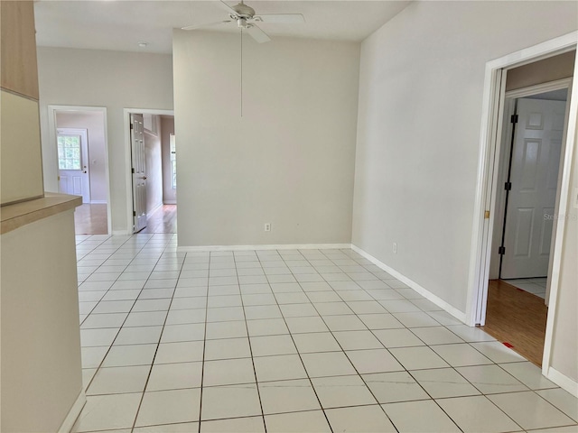 empty room with light tile patterned flooring, a ceiling fan, and baseboards