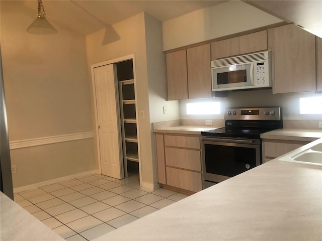 kitchen featuring light tile patterned floors, white microwave, stainless steel electric range oven, hanging light fixtures, and light countertops