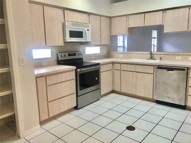 kitchen with appliances with stainless steel finishes, light countertops, a sink, and light brown cabinets