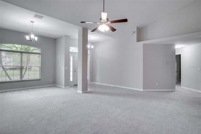 carpeted empty room with high vaulted ceiling and ceiling fan with notable chandelier