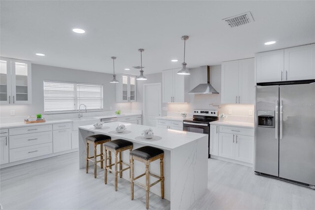 kitchen with appliances with stainless steel finishes, hanging light fixtures, wall chimney exhaust hood, and white cabinets