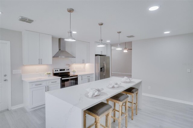 kitchen with stainless steel appliances, decorative light fixtures, white cabinetry, wall chimney exhaust hood, and light wood-type flooring