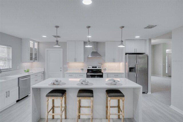 kitchen with wall chimney exhaust hood, a kitchen bar, appliances with stainless steel finishes, and a center island