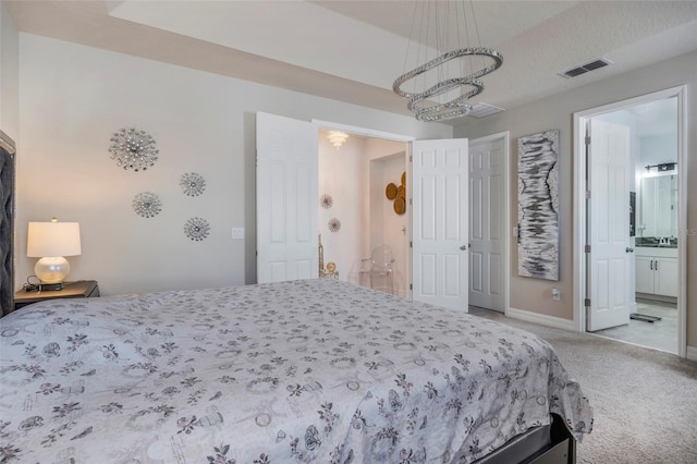 bedroom featuring a textured ceiling, a notable chandelier, light colored carpet, and ensuite bathroom