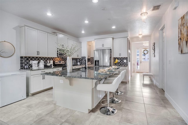 kitchen featuring a kitchen bar, appliances with stainless steel finishes, a center island with sink, and white cabinetry