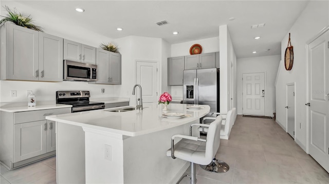 kitchen with stainless steel appliances, a center island with sink, a sink, and light countertops