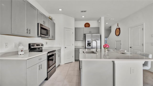 kitchen with light tile patterned floors, an island with sink, appliances with stainless steel finishes, light countertops, and a sink