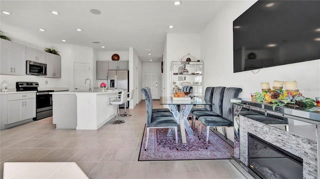 kitchen with appliances with stainless steel finishes, a breakfast bar area, a kitchen island with sink, light countertops, and light tile patterned flooring