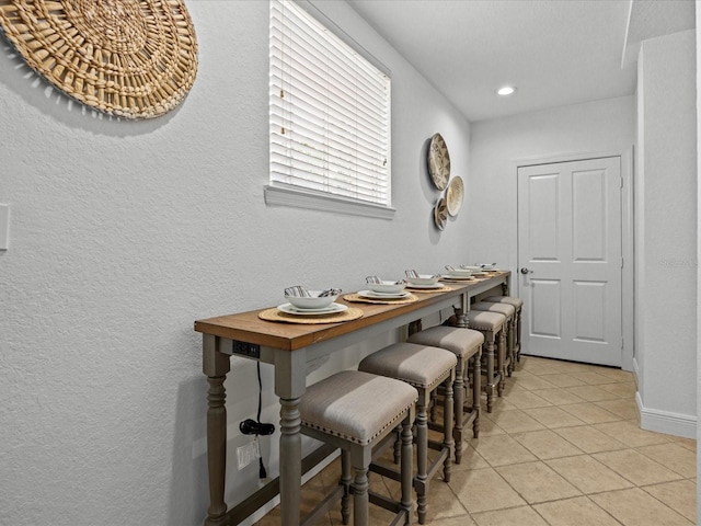 dining area featuring light tile patterned floors, a textured wall, recessed lighting, and baseboards