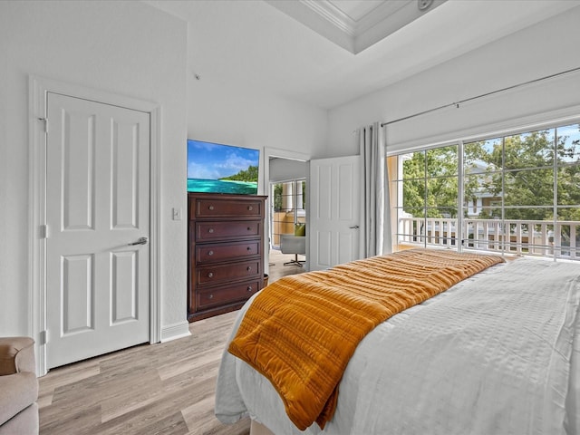 bedroom featuring access to exterior, crown molding, a tray ceiling, and light wood-style floors