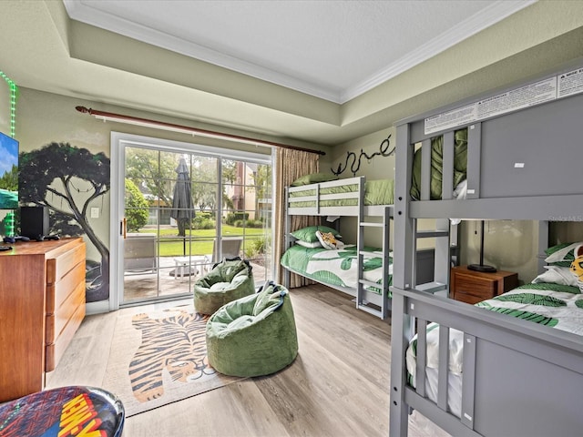 bedroom featuring light wood-style floors, access to outside, crown molding, and a tray ceiling