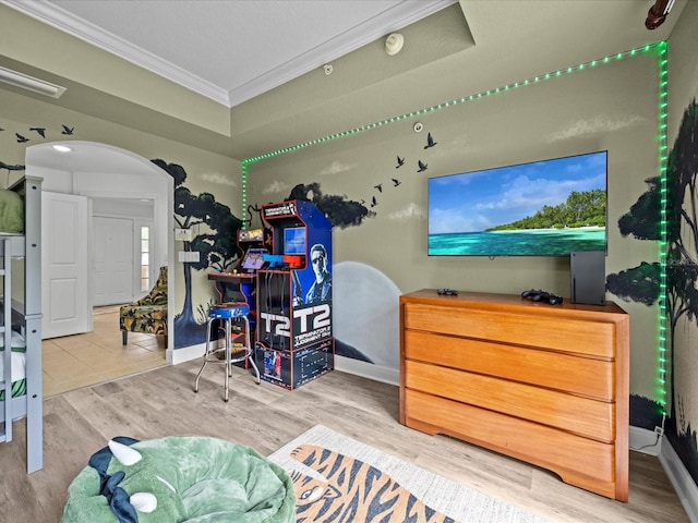 recreation room with baseboards, arched walkways, a raised ceiling, wood finished floors, and crown molding